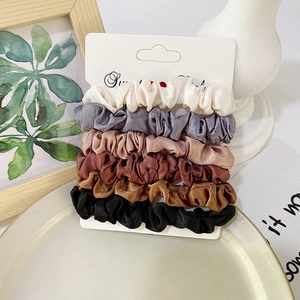 Detail view of 6 colorful satin scrunchies displayed on card in warm aesthetic setting