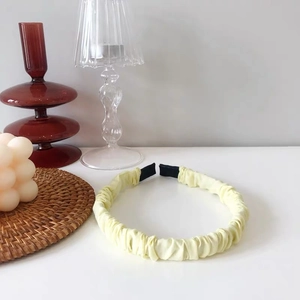 Detail of light yellow ruched headband with satin texture on a stylish white desk