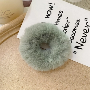 Detailed texture of a soft sage green faux rabbit fur scrunchie on a decorative tray