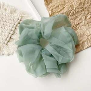 Detail von zartem bohnen-grünem Organza Haargummi mit eleganter Faltenstruktur auf Weiß