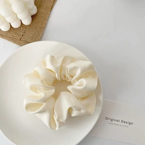 Detailed macro shot of a cream satin scrunchie styled on a white ceramic plate