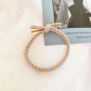 Detail of pink and yellow braided hair tie on textured fabric with a magazine backdrop