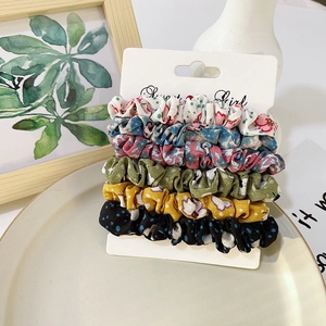 Close-up of five colorful satin scrunchies with floral and polka dot patterns on display