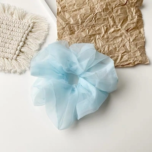 Detailaufnahme eines hellblauen Organza-Haargummis mit weicher Textur auf weißem Stoff