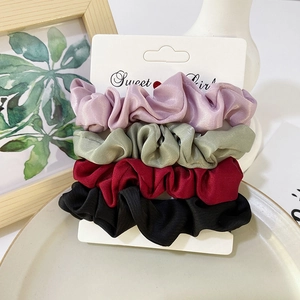 Detailed view of four colorful satin scrunchies displayed on a branded card