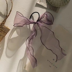Detail view of light purple organza bow hair tie with long ribbons on a textured backdrop