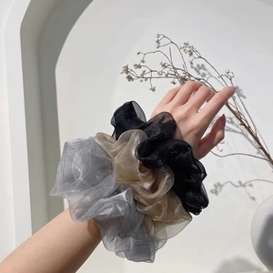 Drei Oversized-Organza-Scrunchies in Grau, Gold und Schwarz am Handgelenk
