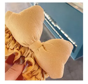 Detail of a mustard yellow bow headband with soft suede texture and ruched fabric design
