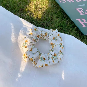 Detailansicht eines Blumen-Haargummis mit gelbem Muster auf weißem Chiffon-Stoff