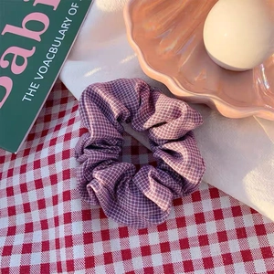 Detailaufnahme eines lila karierten Haargummis mit Retro-Blumen-Ästhetik auf einem Tischtuch
