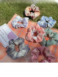 Seven sets of colorful plaid fabric scrunchies displayed on grass during a picnic