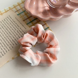 Classic orange and white plaid scrunchie hair tie on a decorative aesthetic background