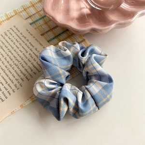 Detail of blue and apricot checkered hair scrunchie on a pink shell ceramic plate