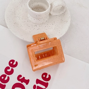 Détail de la pince à cheveux carrée orange avec texture tachetée et design ajouré