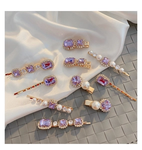 Detail view of purple rhinestone hair clips with pearls on a soft white silk background