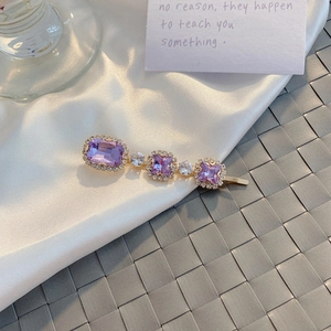 Close-up of vintage purple crystal hair clip with small white zircons on golden metal base