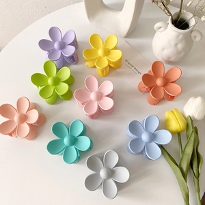 Matte Haarklammern in Blumenform in acht Pastellfarben auf einem weißen Schreibtisch