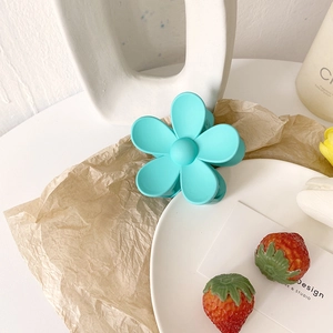 Makroaufnahme einer mattblauen Haarklammer in Blumenform mit Textur auf Kunstpapier