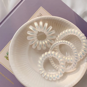 Set of 4 matte iridescent spiral hair ties in a decorative white ceramic bowl