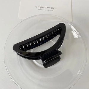 Detailed close-up of a glossy black hollow hair claw clip placed on a glass plate