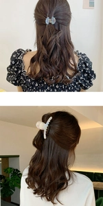 Détail de pinces à cheveux en acétate nacré et marbré sur des cheveux châtains bouclés