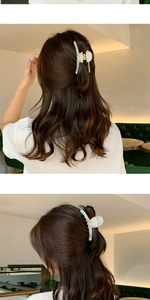 Détail d'une grande pince à cheveux en acétate blanc nacré sur cheveux bruns ondulés