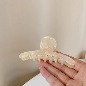 Détail d'une grande pince à cheveux en acétate marbré crème avec une finition brillante
