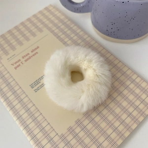 Close-up of white plush hair tie on a pink notebook showing soft faux fur texture