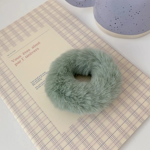 Close-up of soft light green plush hair tie displayed on a yellow plaid notebook