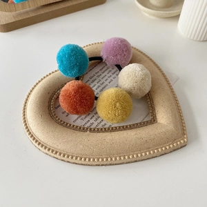 Detail of five colorful plush pom pom hair ties on a heart-shaped wooden prop