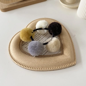 Detailed close-up of colorful plush pom-pom hair ties in a decorative heart tray