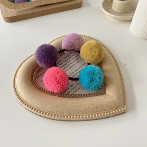 Detailed macro view of colorful soft plush pom-pom hair ties in a decorative heart-shaped tray