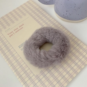 Detail of plush faux fur hair tie in dusty purple on a plaid notebook background