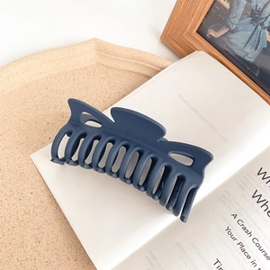 Detail of navy blue matte hair claw clip with cross-tooth design on a white book page