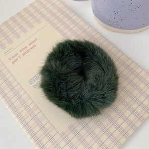 Detailed macro view of a dark green plush scrunchie on a soft pink checkered notebook