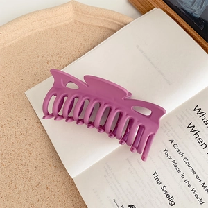 Detail of a large matte purple hair claw clip on an open book for long hair styling