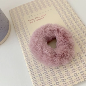Close-up of a soft pink plush scrunchie showing faux fur texture on a grid notebook
