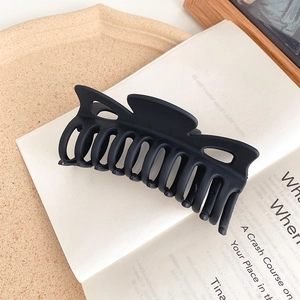 Detail of large matte black shark hair claw clip resting on a minimal cream tray
