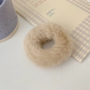 Detailed view of plush beige faux fur scrunchie on stylish magazine background