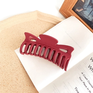 Deep red matte hair claw clip with elegant bow shape on vintage book background