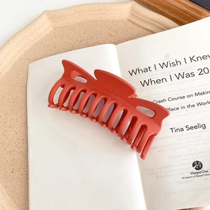 Detail of a matte orange hair claw clip on an open book for versatile hair styling