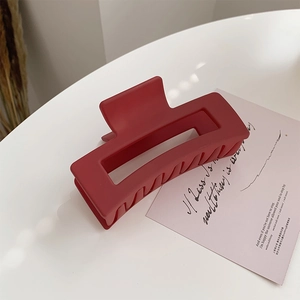 Detail of large matte dark red rectangular hair claw clip with floral accent and artistic card