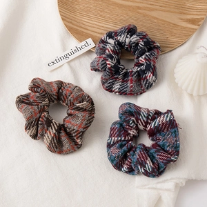 Close-up of three vintage plaid tweed scrunchies on a wooden tray with a cozy candle