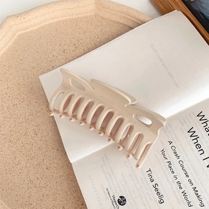 Detail view of large matte beige shark hair claw clip on an open book for styling