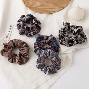 Detail view of five vintage plaid plush hair scrunchies in various retro color patterns