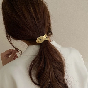Détail d'un élastique à cheveux doré torsadé sur une femme aux cheveux bruns