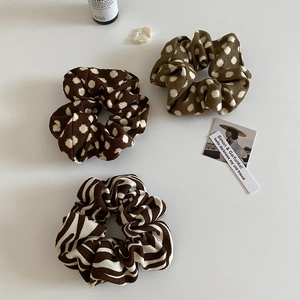 Detailed view of three fabric scrunchies with brown dots and zebra stripes on white background