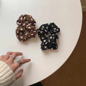 Detail showing two knitted polka dot scrunchies in brown and black on a white surface