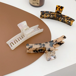 Three large elegant hair claw clips in tortoiseshell and marble patterns on white table