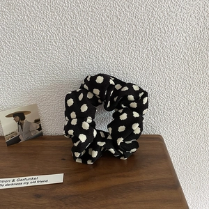 Close-up of a classic black scrunchie with white polka dots on a rustic wooden background